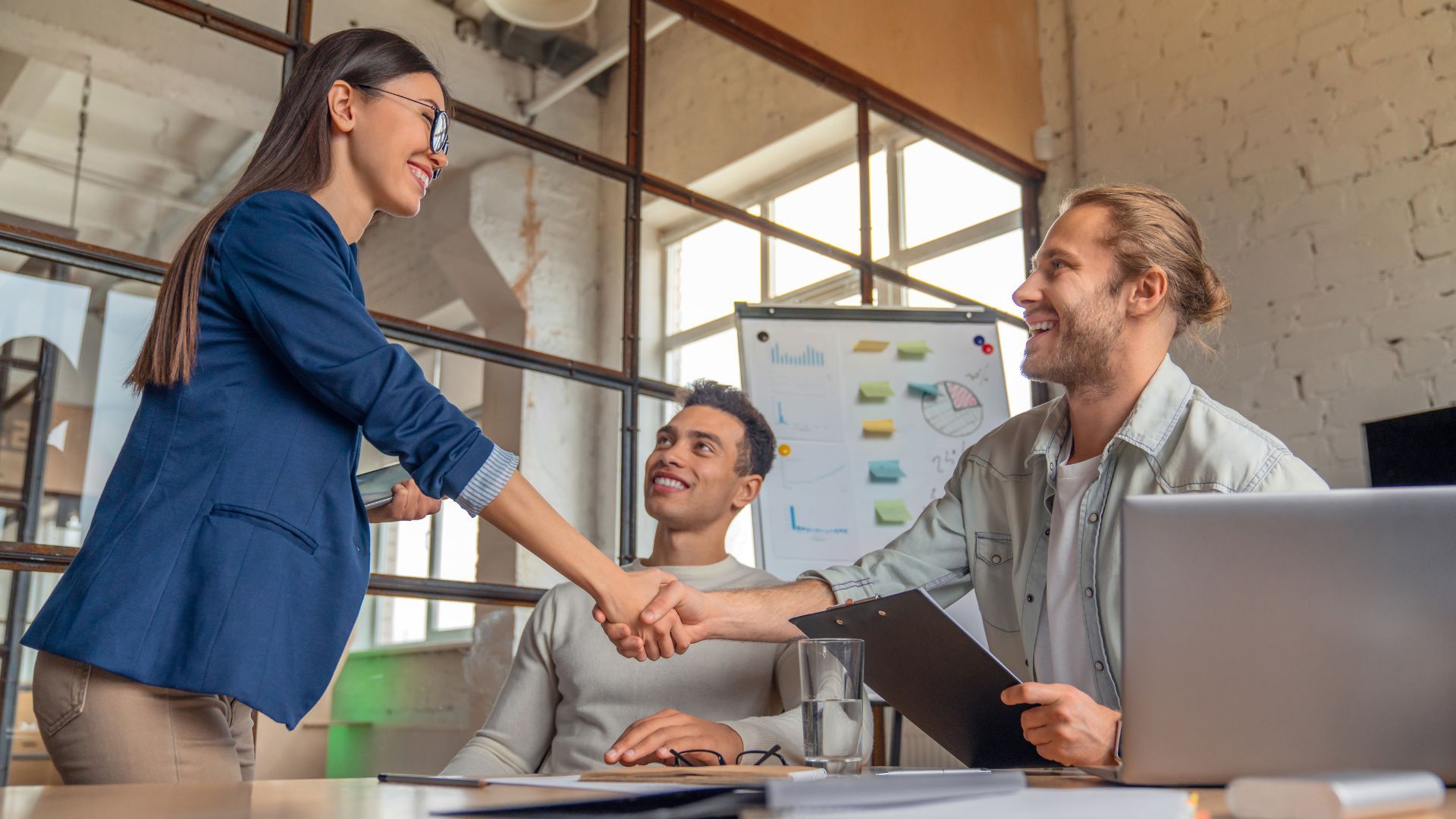 Smiling colleagues shaking hands in a modern office setting.
