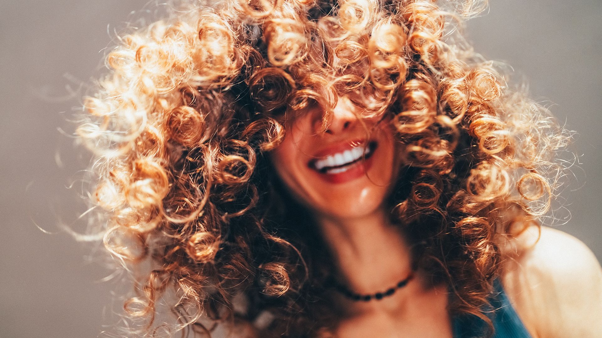 Smiling woman with voluminous curly hair covering her eyes